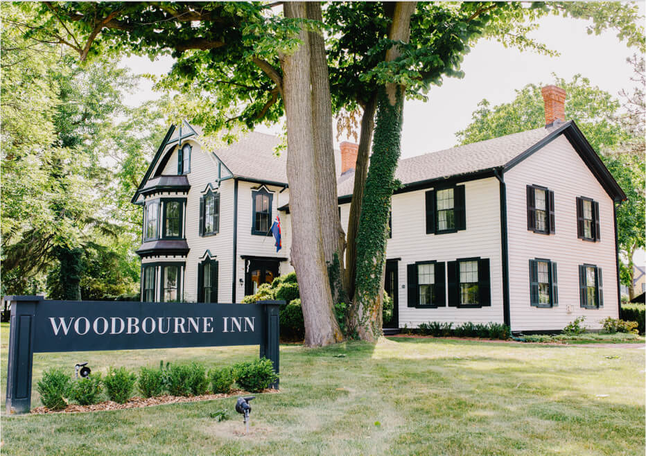 Exterior of The Woodbourne Inn with its sign, surrounded by mature trees