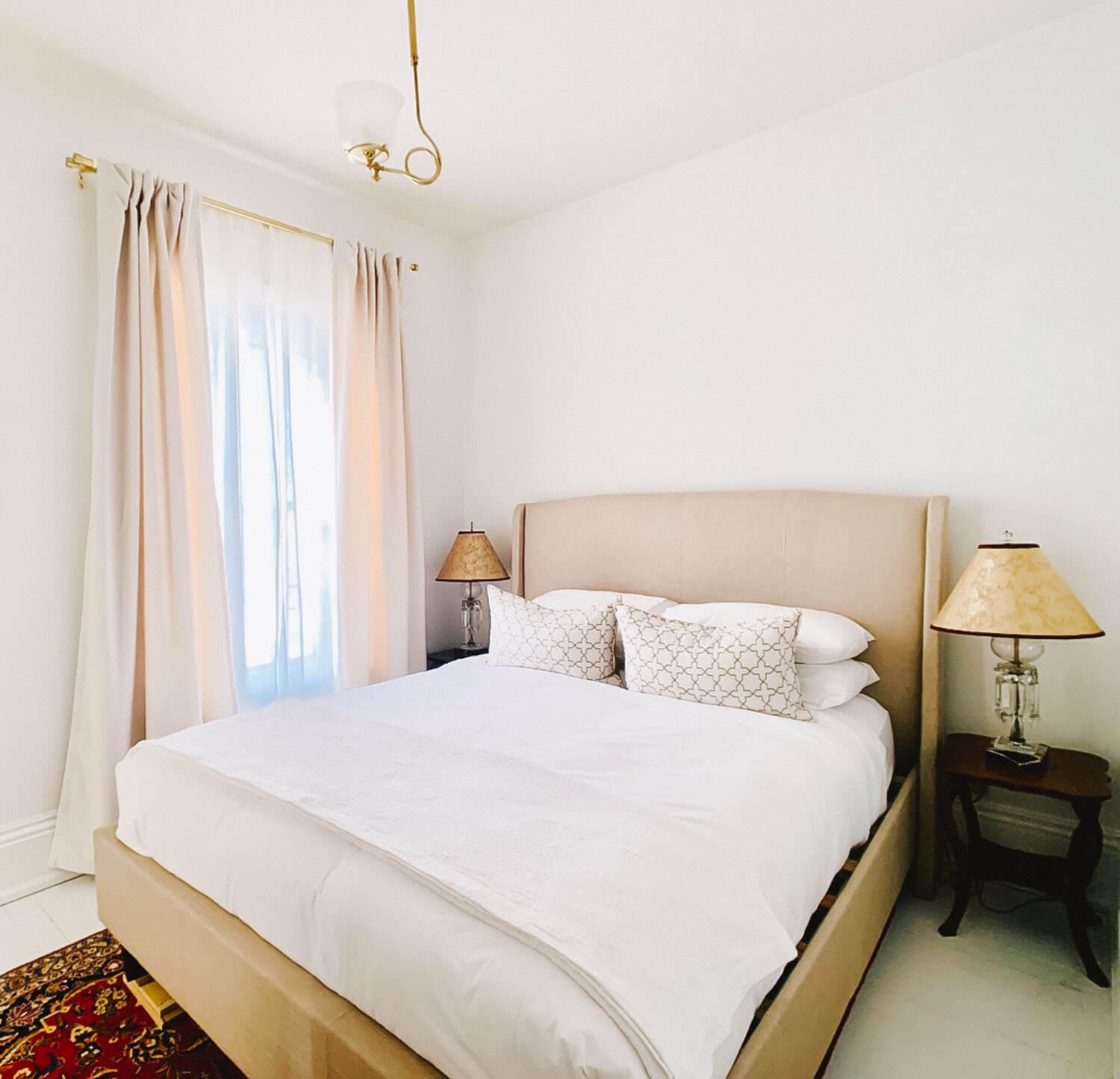 Bedroom with a cream upholstered headboard and blush curtains