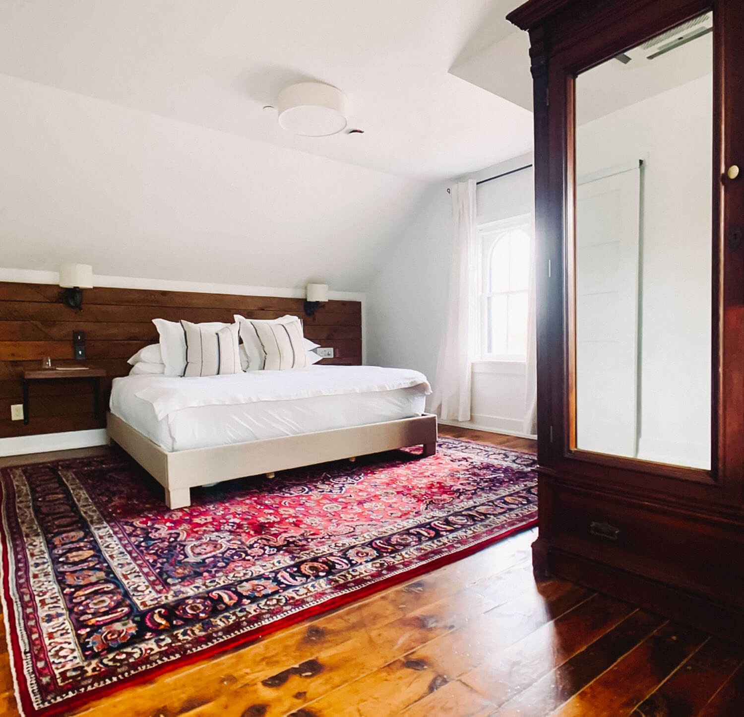 Attic bedroom with a wood-paneled accent wall and an antique mirrored wardrobe