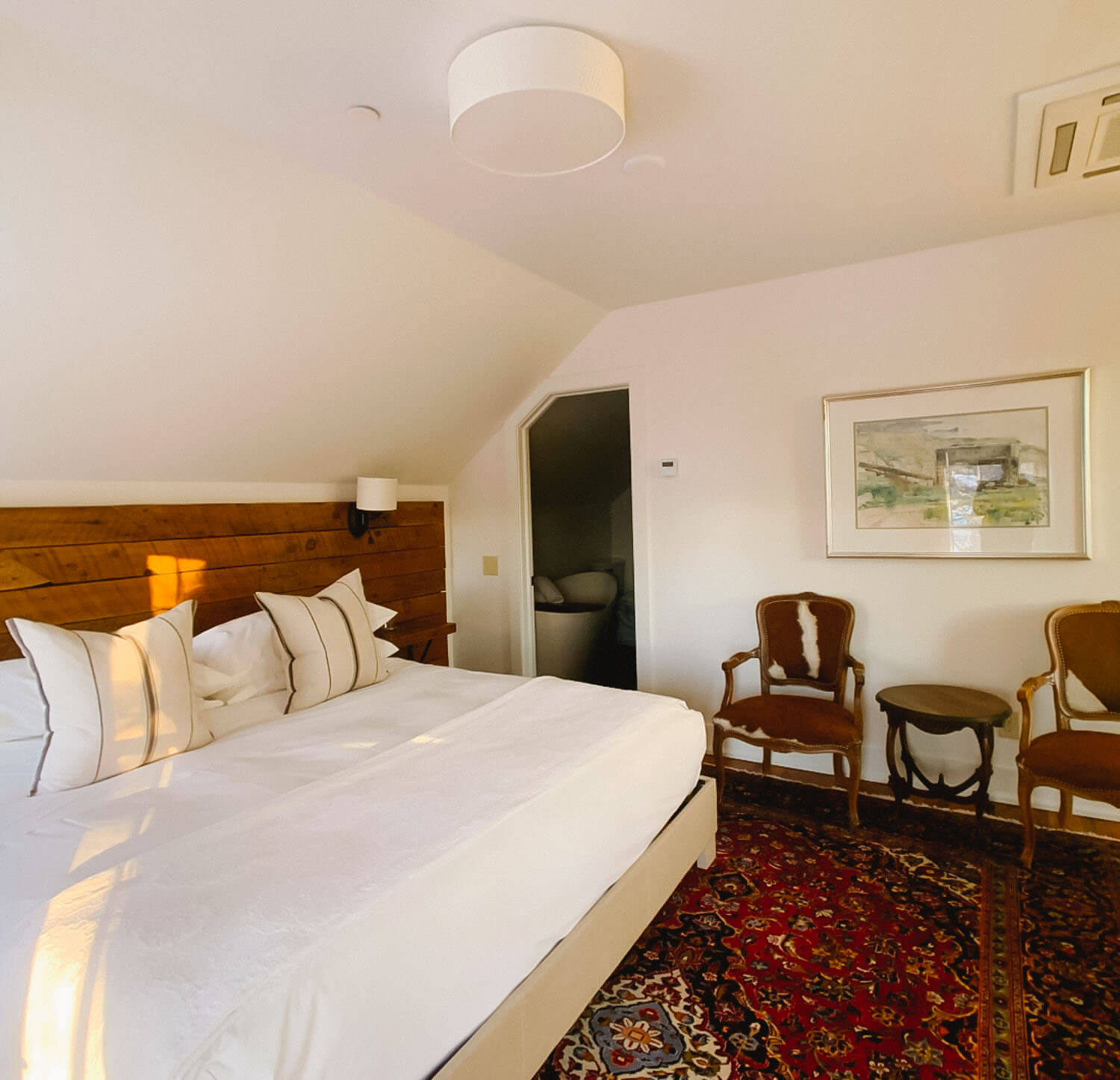 Attic bedroom with a wood-paneled accent wall and cowhide-upholstered accent chairs